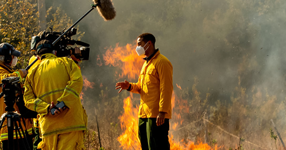 Reporter making a report with flames from wildfire behind them